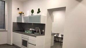 Uma cozinha moderna com armários brancos, forno embutido, pia e máquina de café. Há duas plantas em vasos sobre a bancada.