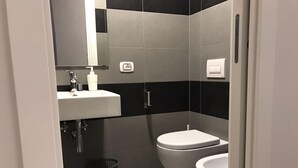 Casa de banho moderna com lavatório branco, espelho e duas sanitas.