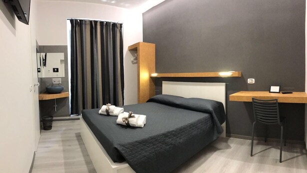 Quarto de hotel moderno com cama, escrivaninha, cadeira e chuveiro.