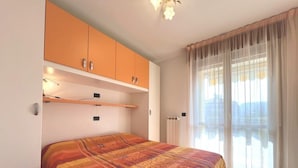 A bedroom with a bed, orange cabinets, a radiator, and a window with curtains. - Peaceful Retreat in Grado Close to the Beach (Grado)