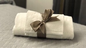 A neatly folded white towel with a brown bow, placed on a textured surface. - Economy Room for 1  2 people Piazza San Giovanni (ROMA)
