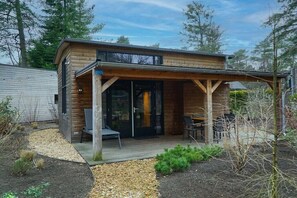 A wooden cabin with a covered patio, a sliding glass door entrance, and a small outdoor seating area. - Holiday home in Beekbergen with terrace (Beekbergen)