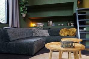 A modern living room with a dark green sofa, a wooden coffee table, and a bookshelf with decorative items. - Holiday home in Beekbergen with terrace (Beekbergen)