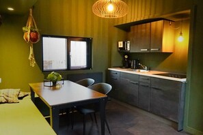 A compact kitchen with a dining area, a hanging plant, and a window with blinds. - Holiday home in Beekbergen with terrace (Beekbergen)