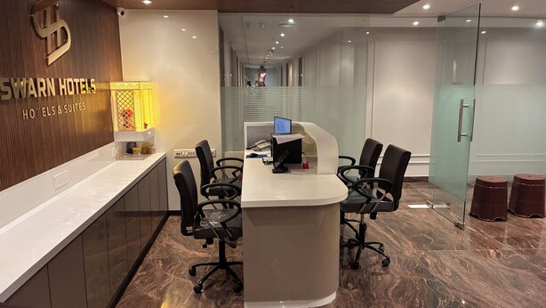 Un mostrador de recepción de hotel con diseño moderno, una computadora y un área de descanso con sillas.