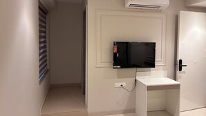 Una habitación con una televisión de pantalla plana montada en la pared, una puerta blanca y un equipo de aire acondicionado.