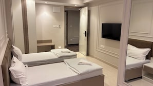A hotel room with two beds, a TV, a mirror, and a door leading to a hallway. - Swarn Hotel (Kolkata)