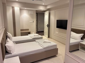 A hotel room with two beds, a TV, a mirror, and a door leading to a hallway. - Swarn Hotel (Kolkata)