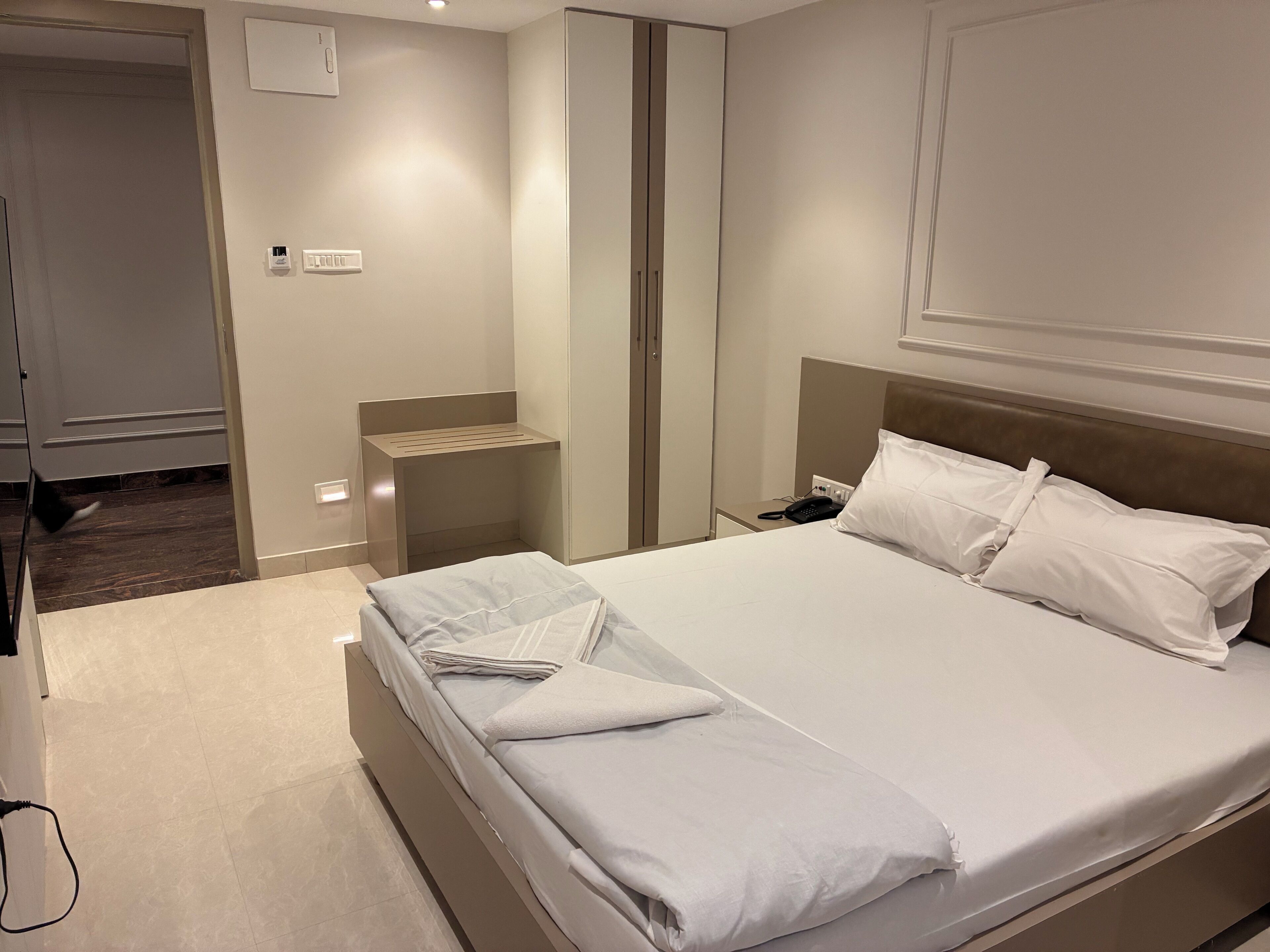 Quarto de hotel com cama bem arrumada, mesa de cabeceira com telefone e luminária na parede.