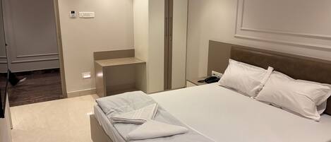 Quarto de hotel com cama bem arrumada, mesa de cabeceira com telefone e luminária na parede.