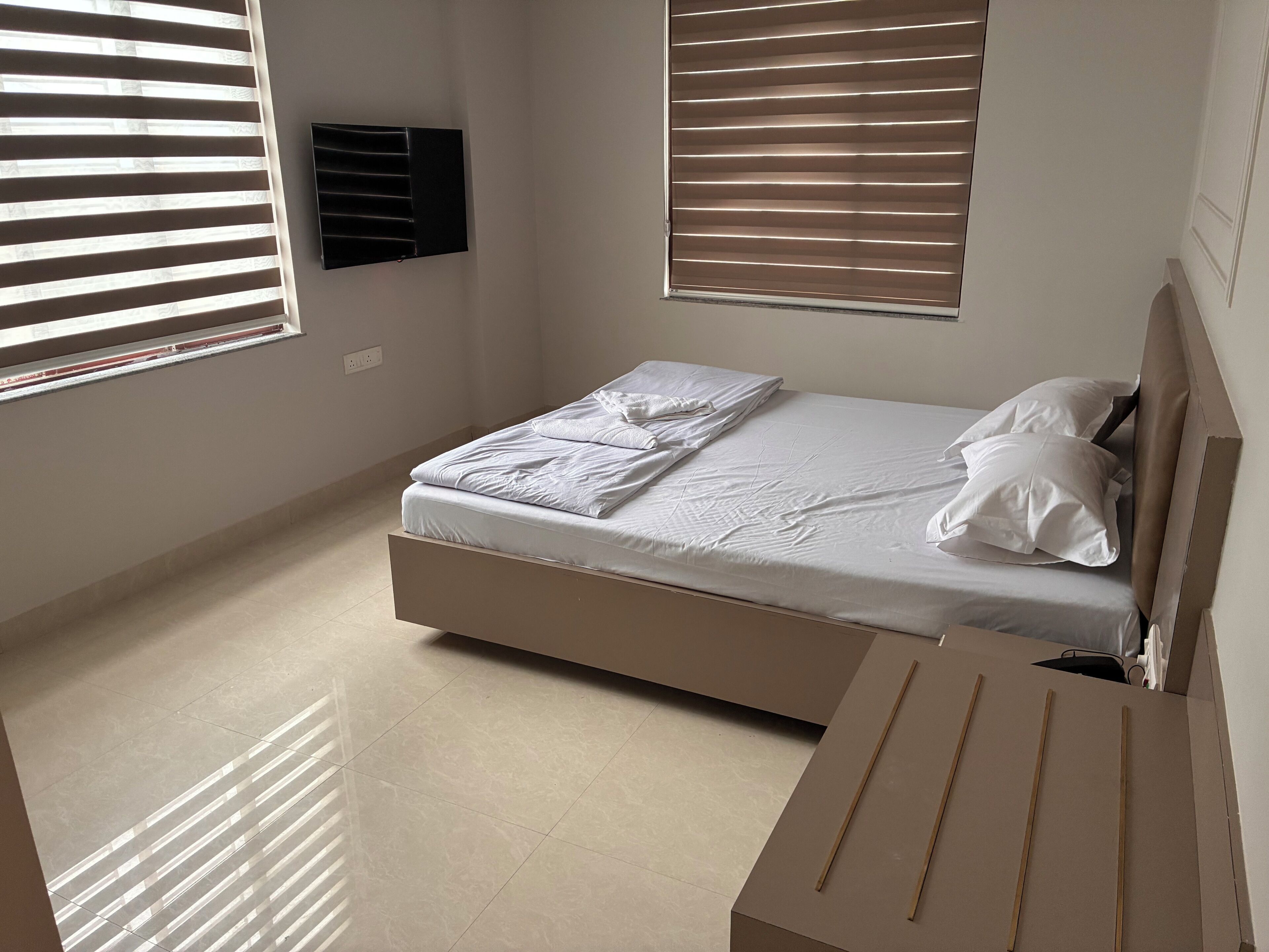 A bedroom with a bed, two windows with blinds, a wall-mounted air conditioner, and a tiled floor.