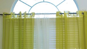 A room with a bed, yellow curtains, and a window with blinds. - Adorable 2-bedroom bungalow with AC in St. Catherine Parish (St. Catherine Parish)