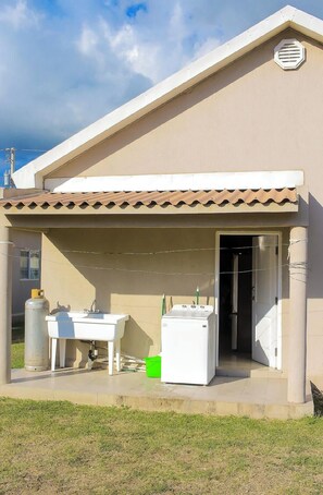 Ein Gebäude mit überdachter Außenbereitschaft, einem Waschbecken, einer Waschmaschine und einer Gasflasche.