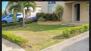 A residential area with a well-maintained lawn, a palm tree, and a car parked in the driveway. - Adorable 2-bedroom bungalow with AC in St. Catherine Parish (St. Catherine Parish)