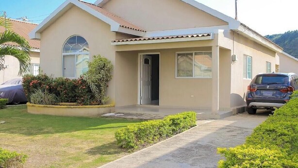 A single-story house with a front door, a small porch, and a car parked in the driveway. - Adorable 2-bedroom bungalow with AC in St. Catherine Parish (St. Catherine Parish)