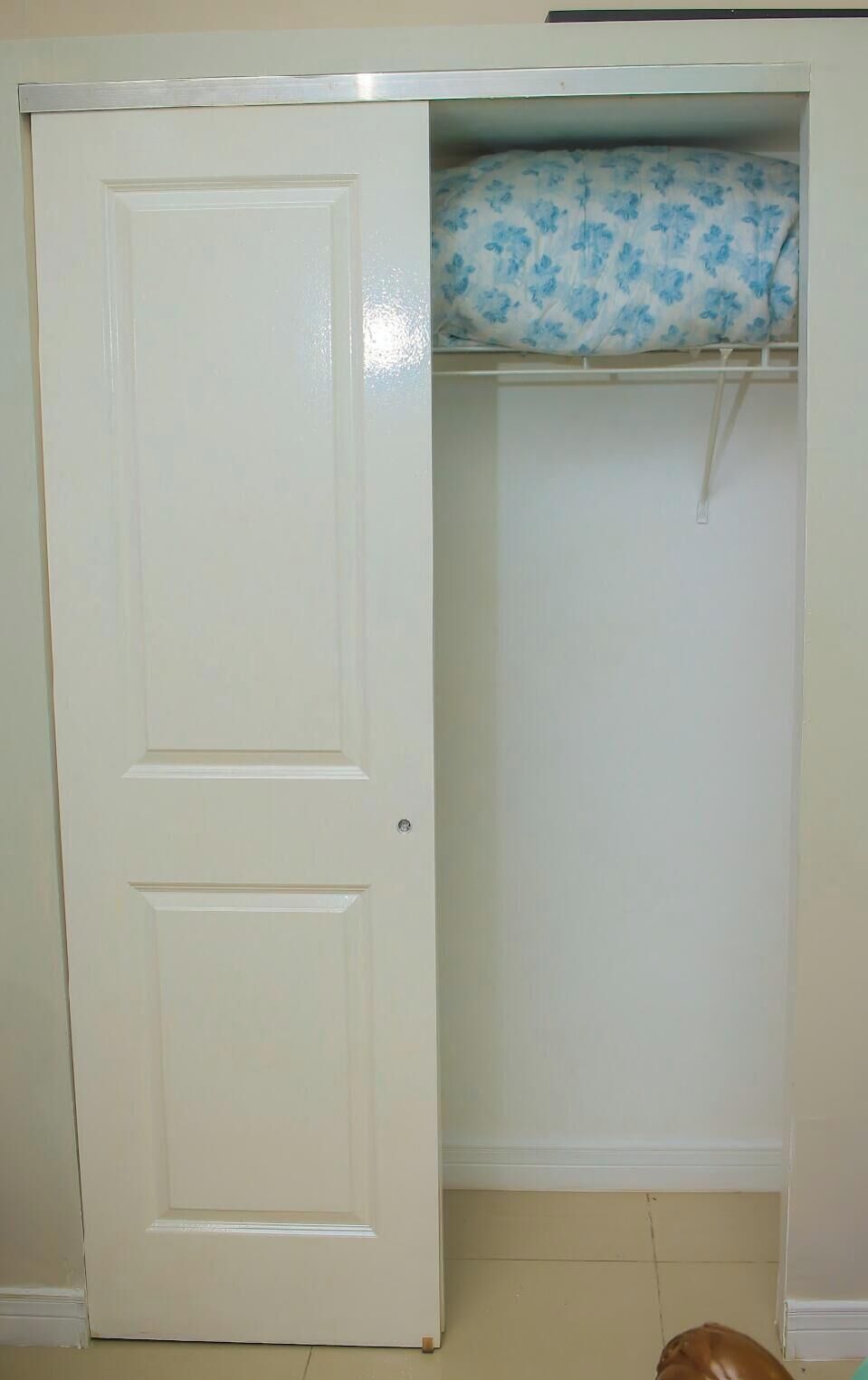 A closed white door with a closet containing a blue floral bedspread.
