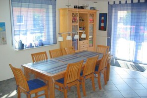 Ein Essbereich mit Tisch und Stühlen, eine Holzkabine mit Glastüren und ein Fenster mit Vorhängen.