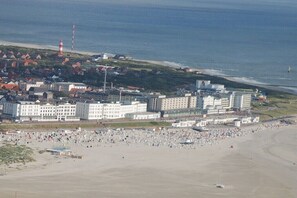 Eine Küstenstadt mit einem breiten Strand, einem Leuchtturm und einem markanten Hotel mit mehreren Gebäuden.