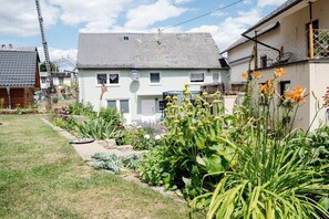 Ein Wohngebiet mit Häusern, einem Garten mit verschiedenen Pflanzen und einer Satellitenschüssel an einem der Häuser.