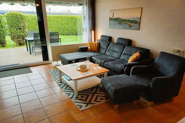 Ein modernes Wohnzimmer mit Sofa, Hocker und Couchtisch, einem Gemälde an der Wand und Blick ins Freie.