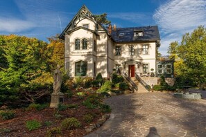 Ein großes, historisches Gebäude mit einer markanten Fassade, einer Statue im Garten und einem gepflegten Steinweg.