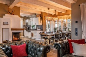 Ein gemütliches Wohnzimmer mit Kamin, Ledersofas und einem Essbereich mit Küche im Hintergrund.