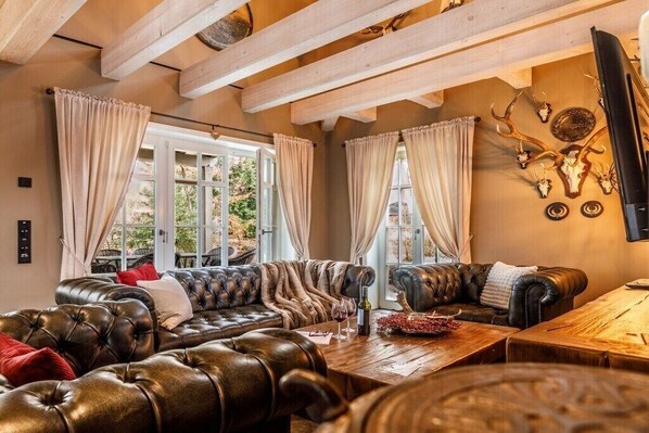 Ein gemütliches Zimmer mit einem Ledersofa, einem Holztisch und einem großen Fenster mit Vorhängen.