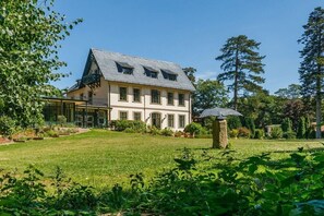 A large, two-story house with a sloped roof, surrounded by a well-maintained lawn and trees.