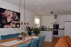 Eine moderne Küche mit einer zentralen Kochinsel, einem Essbereich mit Türkis-Stühlen und einem großen Blumenbild an der Wand.