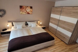Ein Schlafzimmer mit einem großen Bett, Nachttischen, einem Kleiderschrank und einem an der Wand hängenden Kunstwerk.