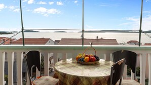 A balcony with a table and chairs, a fruit basket, and a view of a body of water and buildings. - Angelo Apartment Brodarica 1 (Šibenik-Brodarica)