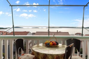 A balcony with a table and chairs, a fruit basket, and a view of a body of water and buildings. - Angelo Apartment Brodarica 1 (Šibenik-Brodarica)