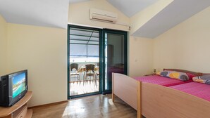 A bedroom with a bed, a TV, a sliding glass door leading to a balcony, and an air conditioning unit. - Angelo Apartment Brodarica 1 (Šibenik-Brodarica)