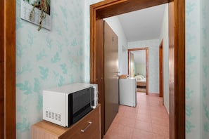Ein Flur mit einer Mikrowelle auf einem Holzschrank, einem Kühlschrank und einer Tür zu einem anderen Zimmer.