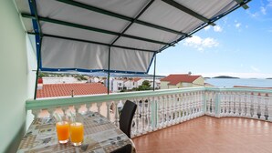 En balkong med ett bord, två drinkar och utsikt över havet och byggnaderna.