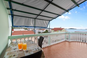 Ein Balkon mit Tisch, zwei Getränken und Blick auf das Meer und die Gebäude.