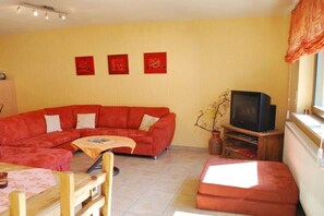 Ein Wohnzimmer mit einem roten Sofa, einem Holztisch, einem Fernseher auf einem Holzständer und drei roten Wandbildern.
