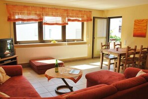 Ein Wohnzimmer mit einer Couch, einem kleinen runden Tisch mit einer Flasche und Gläsern, einem Fernseher und einem Essbereich mit Stühlen und einem Tisch.