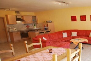 A compact living space with a kitchen, a red sofa, a dining table, and a TV. - Premium Winery Leo Klaus (Ernst)