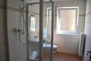 Ein Badezimmer mit Glasdusche, Waschbecken, Toilette und Fenster.