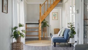 Eine Treppe, die zu einer oberen Etage führt, ein blaues Sofa und ein runder Teppich in einem hellen Raum mit Tageslicht.
