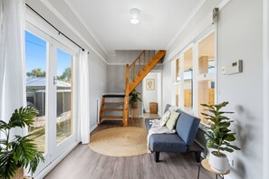 A spacious living area with a staircase, a sofa, and large windows.