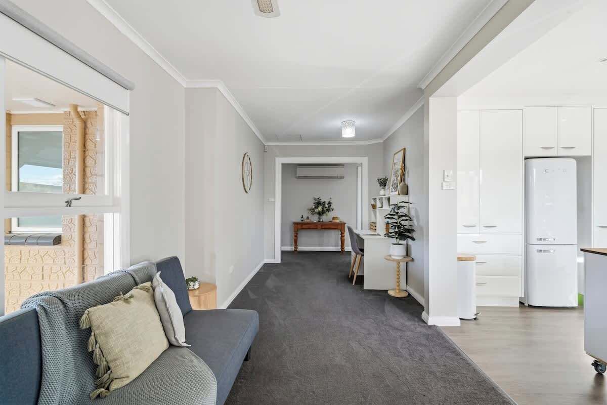 A modern living room with a grey sofa, a small table, and a kitchen area with white cabinets and a refrigerator.