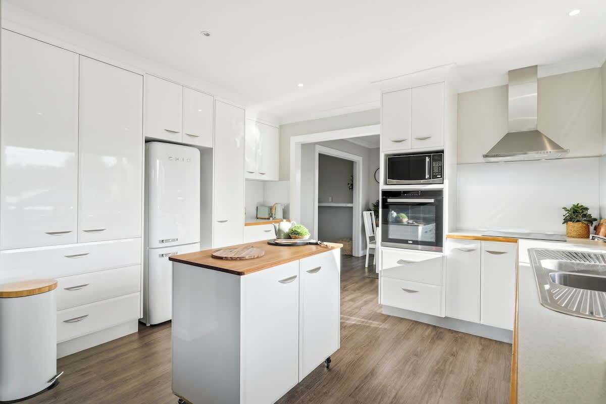 A modern kitchen with white cabinetry, a central island, a microwave, and an oven.