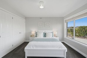 A bedroom with a white bed, two bedside tables with lamps, a large window with a view, and a ceiling light fixture. - Perfect For Families and Small Groups (Legana)