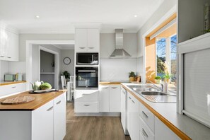 Une cuisine moderne avec des meubles blancs, un four encastré, un four à micro-ondes et une fenêtre donnant sur l’extérieur.