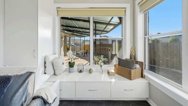Ein modernes Zimmer mit einem großen Fenster, einer weißen Bank mit Kissen und Blick ins Freie.