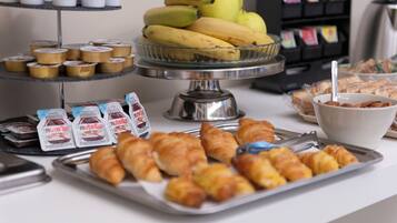 A buffet with various food items including bananas, pastries, and packaged snacks.