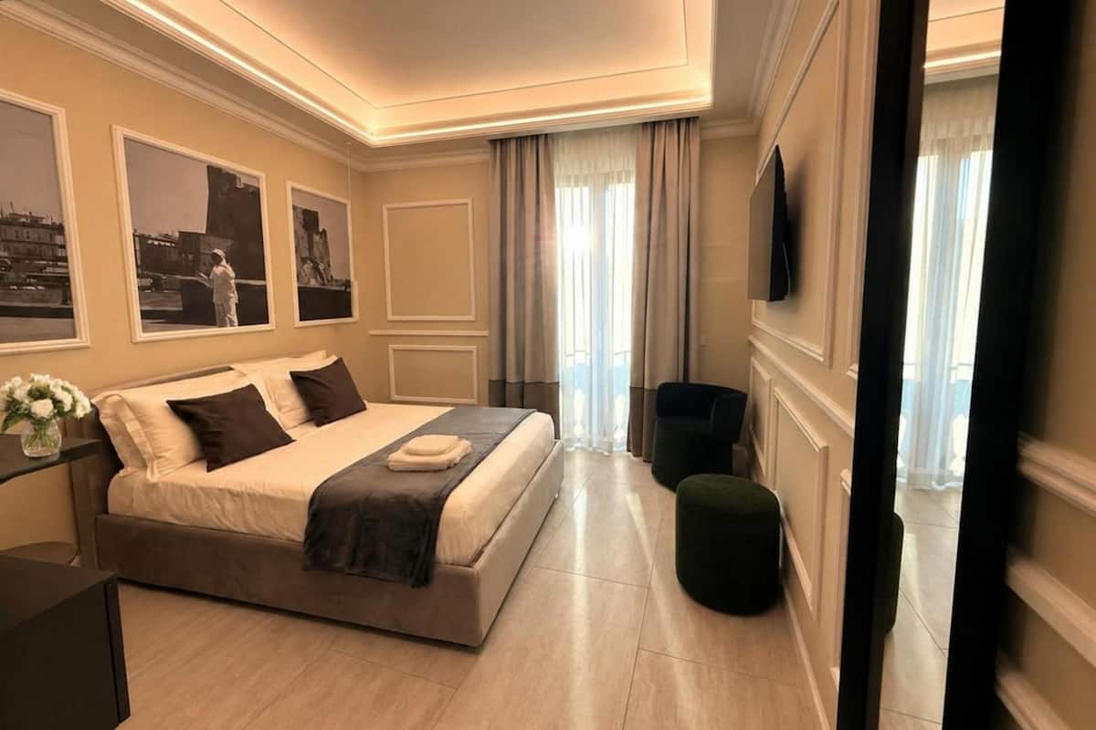 A hotel room with a bed, a desk, a chair, a TV, and a window with curtains.