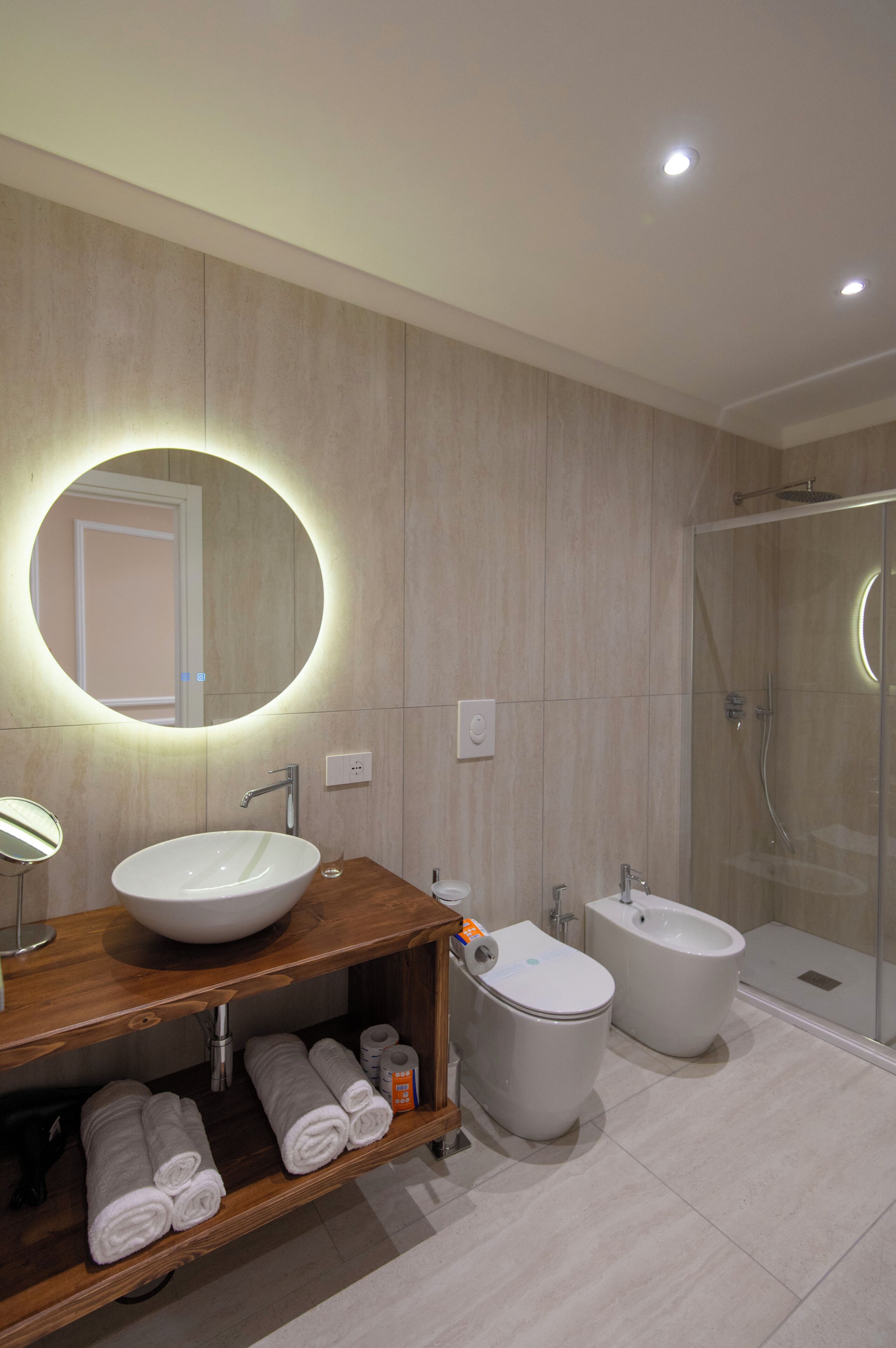 A modern bathroom with a round mirror, a sink, a bidet, and a shower.